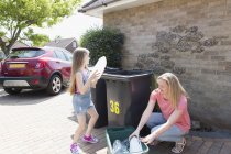 Madre e hija reciclando plástico fuera de casa - foto de stock