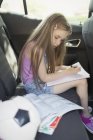 Menina fazendo lição de casa no banco de trás do carro — Fotografia de Stock
