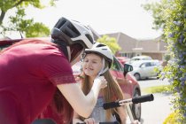 Mãe capacete de fixação na filha montando scooter na entrada ensolarada — Fotografia de Stock