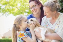 Affectionate lesbian couple and daughter kissing dog — Stock Photo