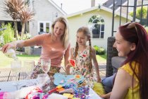 Lesbianas pareja disfrutando de vino blanco y haciendo proyecto de artesanía con hija en patio - foto de stock