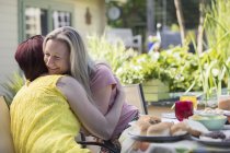 Cariñosa lesbiana pareja abrazando en almuerzo patio mesa - foto de stock