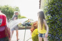 Playful daughter spraying mother with hose in sunny driveway — Stock Photo