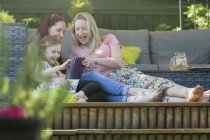 Lesbian couple and daughter using digital tablet on patio — Stock Photo