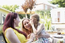 Affectionate lesbian couple holding daughter on sunny patio — Stock Photo