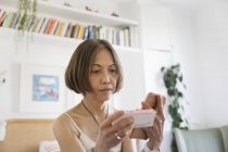 Senior woman with smart phone looking at box of medicine — Stock Photo