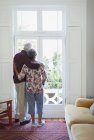 Gelassenes Senioren-Paar blickt aus Wohnzimmerfenster — Stockfoto