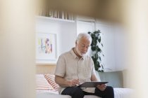 Uomo anziano utilizzando tablet digitale sul letto — Foto stock