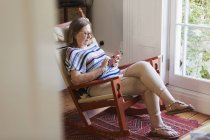 Seniorin textet mit Smartphone im Schaukelstuhl — Stockfoto