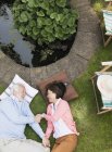 Affectionate senior couple laying by pond in garden — Stock Photo