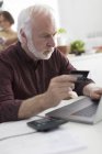 Focalisé senior homme avec carte de crédit payer les factures à l'ordinateur portable — Photo de stock