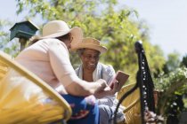 Mujeres amigas mayores usando un teléfono inteligente en un patio soleado - foto de stock
