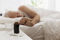 Müder Senior schläft neben Nachttisch mit Hustensaft und Medikamenten — Stockfoto
