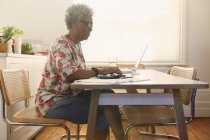Старша жінка платить рахунки в ноутбуці на кухні — стокове фото