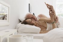 Cariñosa pareja de personas mayores utilizando el teléfono inteligente en la cama - foto de stock