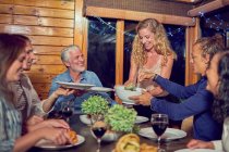 Woman serving dinner to friends at cabin dining table — Stock Photo
