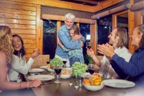 Amigos batendo palmas para casal afetuoso abraçando à mesa de jantar — Fotografia de Stock