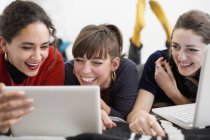 Сміються молоді жінки друзі зависають, насолоджуючись цифровим планшетом і ноутбуком на ліжку — стокове фото