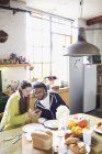 Jeune couple avec téléphone intelligent profiter du petit déjeuner dans la cuisine de l'appartement — Photo de stock