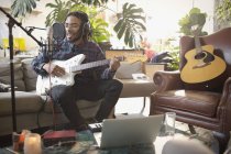 Giovane musicista di sesso maschile che registra musica, suona la chitarra e canta nel microfono in appartamento — Foto stock