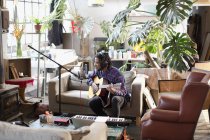 Junger männlicher Musiker nimmt Musik auf, spielt Gitarre und singt in Wohnung ins Mikrofon — Stockfoto