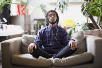 Gelassener junger Mann meditiert mit Kopfhörern auf Wohnungssofa — Stockfoto