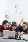 Молодые женщины друзья тусуются, используя цифровые планшеты на кровати — стоковое фото