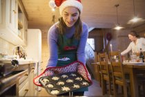 Девочка-подросток в рождественской шляпе Санта-Клауса печет на кухне — стоковое фото