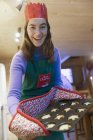 Portrait enthusiastic teenage girl in Christmas apron and paper crown baking muffins — Stock Photo