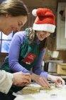 Madre e hija en delantal de Navidad y Santa sombrero de hornear en la cocina - foto de stock