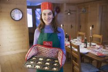 Muchacha adolescente sonriente retrato en delantal de Navidad y la corona de papel hornear magdalenas en la cocina - foto de stock