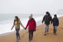 Family in warm clothing walking on snowy winter beach — Stock Photo