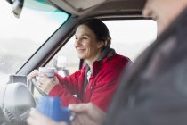 Усміхнена жінка п'є каву і водить двигун додому — стокове фото
