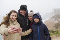 Nieve cayendo sobre la familia tomando selfie con teléfono de la cámara - foto de stock