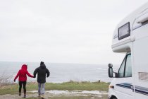 Couple holding hands outside motor home overlooking ocean — Stock Photo
