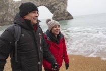 Glückliches Paar in warmer Kleidung am verschneiten Strand des Ozeans — Stockfoto