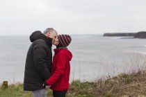 Casal afetuoso beijando no penhasco com vista para o oceano — Fotografia de Stock