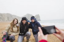 Happy family posing for photograph on snowy winter beach — Stock Photo