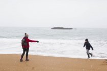 Madre giocherellona e figlio sulla spiaggia innevata dell'oceano invernale — Foto stock