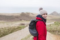 Портрет усміхненої жінки в теплому одязі з рюкзаком, що йде по віддаленому шляху — стокове фото