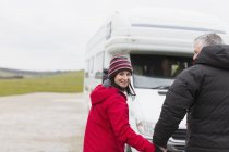 Portrait couple souriant dans des vêtements chauds tenant la main à l'extérieur du camping-car — Photo de stock