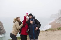 Сім'я з телефоном, що бере селфі на скелі з видом на океан — стокове фото
