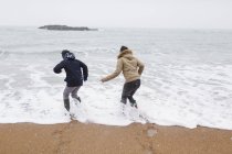 Playful teenage brother and daughter playing in winter ocean surf — Stock Photo