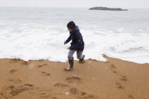 Verspielter Junge spielt in der winterlichen Brandung des Meeres — Stockfoto