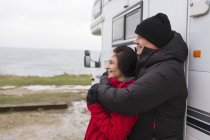Affectionate couple in warm clothing hugging outside motor home — Stock Photo