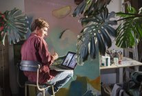 Artista masculino pintando e usando laptop no estúdio de arte — Fotografia de Stock