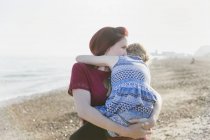 Mãe afetuosa segurando filha na praia ensolarada — Fotografia de Stock