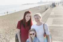 Retrato sonriente lesbiana pareja e hija en soleado playa boardwalk - foto de stock