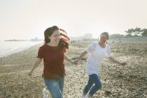 Игривая, ласковая лесбийская пара, держащаяся за руки и бегущая по солнечному пляжу — стоковое фото