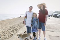 Портрет улыбающейся лесбийской пары с дочерью и собакой на солнечном пляже — стоковое фото